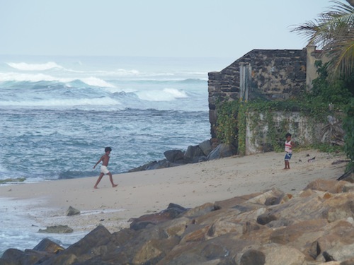 zwei Kinder am Strand bei Mirissa und dahinter tobt das Meer