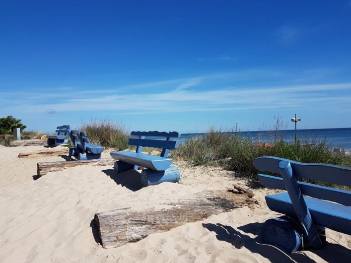 blaue Bänke im Sand und dahinter Blick auf die Ostsee