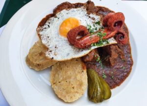 Gulasch mit Würstchen, Spiegelei, Gurke und Knödeln