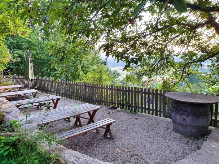 Gastgarten vom Buschenschank Schmallegger mit Biertischen und Bänken und umgeben von Bäumen