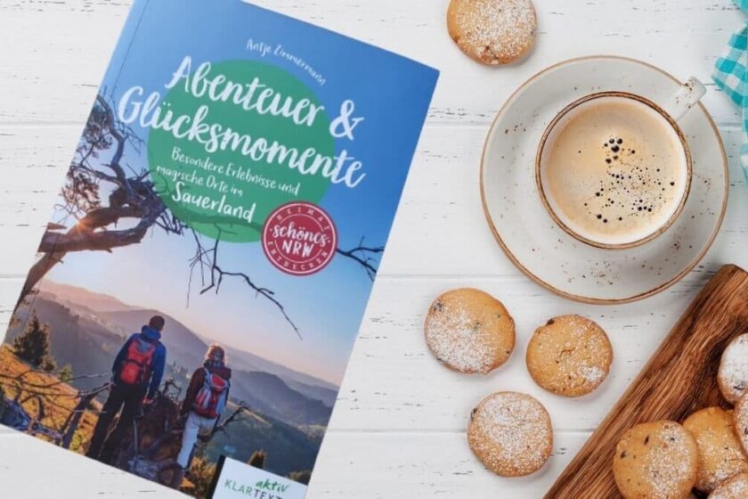 Reiseführer Abenteuer und Glücksmomente neben einer Tasse Kaffee und Keksen
