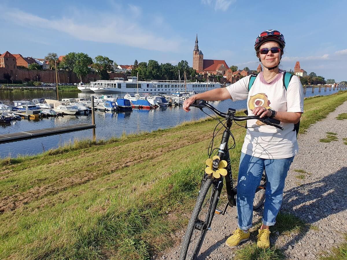 Martina mit dem E-Bike an der Elbe vor der Kulisse von Tangermünde