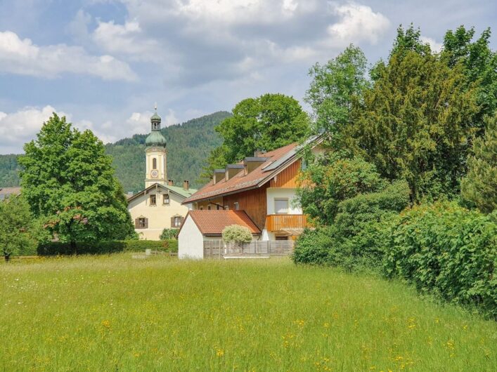 Blick auf die Kirche von Lenggries hinter saftig grünen Wiesen