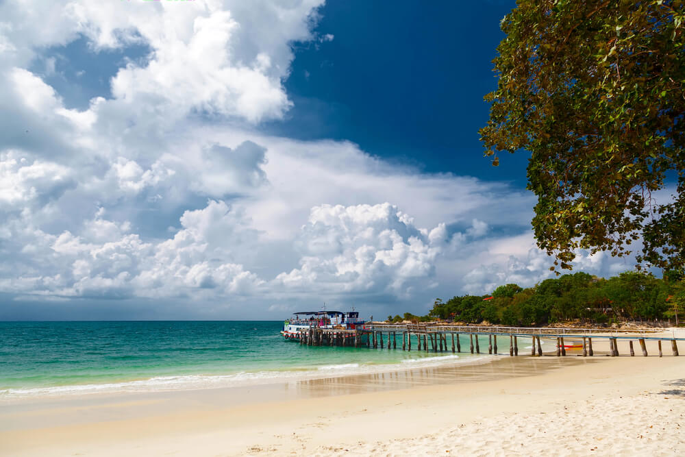 ein schöner Sandstrand auf der Insel Koh Samet, daneben das türkisfarbene Meer mit Blick auf ein Schiff am Anleger