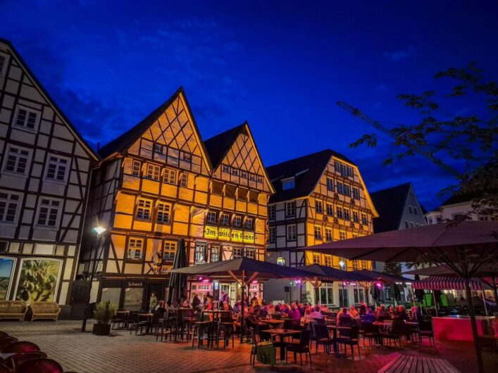 Beleuchtete Fachwerkhäuser in der Altstadt von Soest bei Nacht mit gut besuchter Außengastronomie unter tiefblauem Abendhimmel.