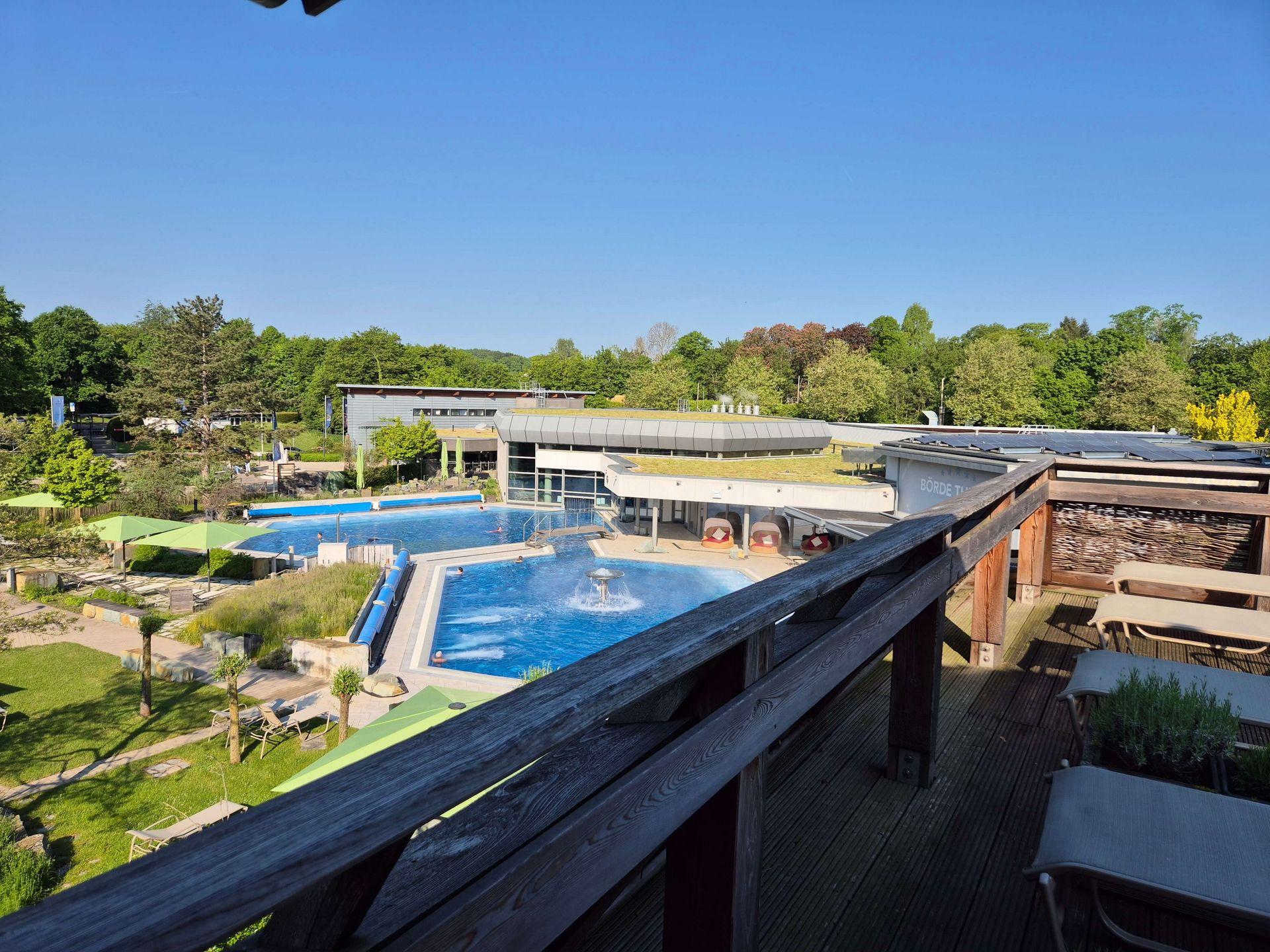 Blick von einer Dachterrasse auf die Außenbecken, Liegewiesen und Gebäude der Börde-Therme in Bad Sassendorf.