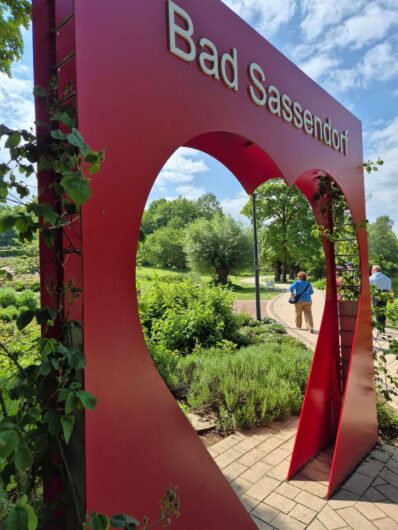 Große rote Herz-Skulptur mit der Aufschrift Bad Sassendorf im Kurpark, durch deren herzförmige Öffnung ein Spazierweg führt.