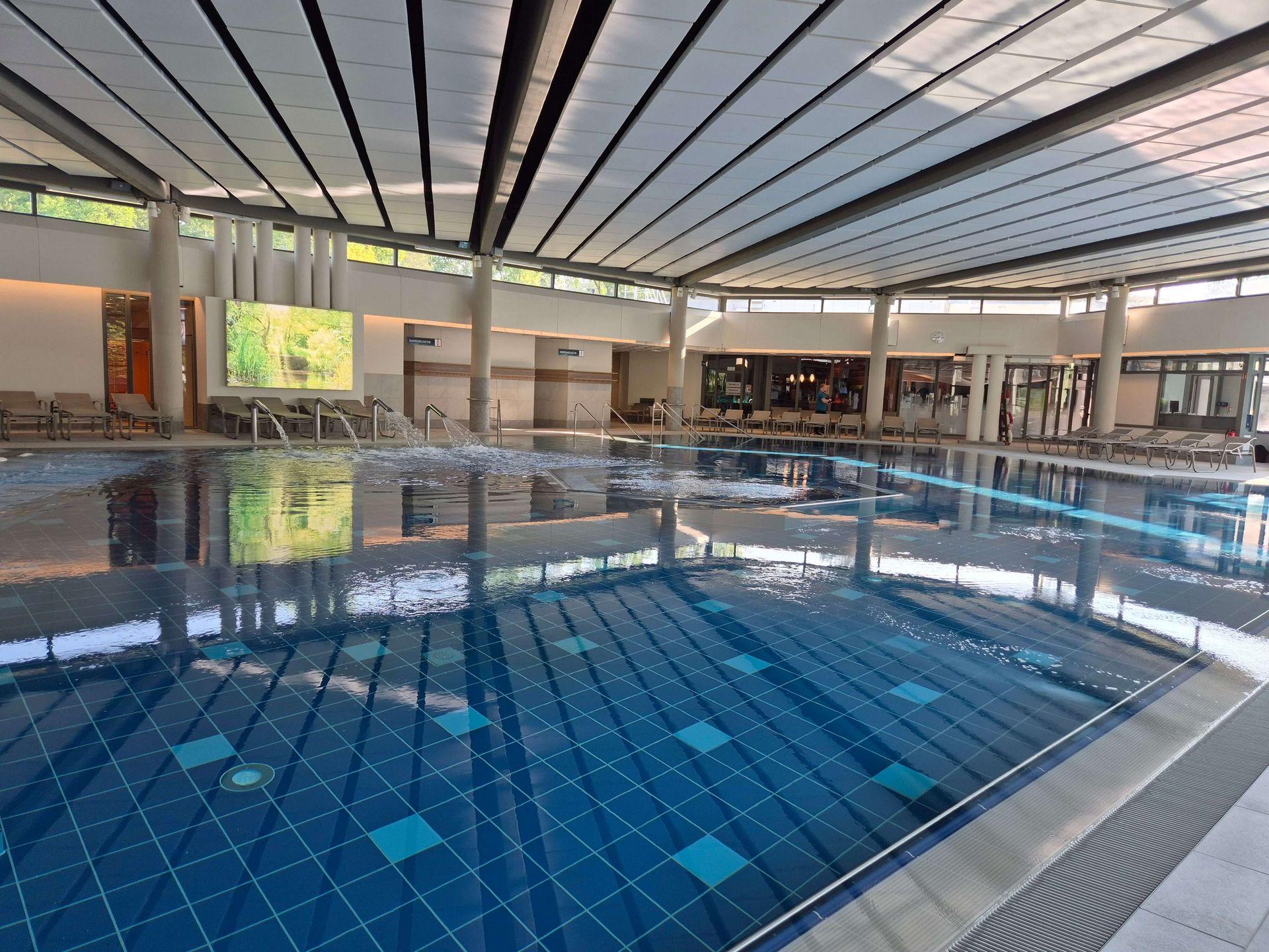 Großes Innenbecken der Börde-Therme Bad Sassendorf mit blau gefliestem Boden, Wasserdüsen und Ruheliegen.