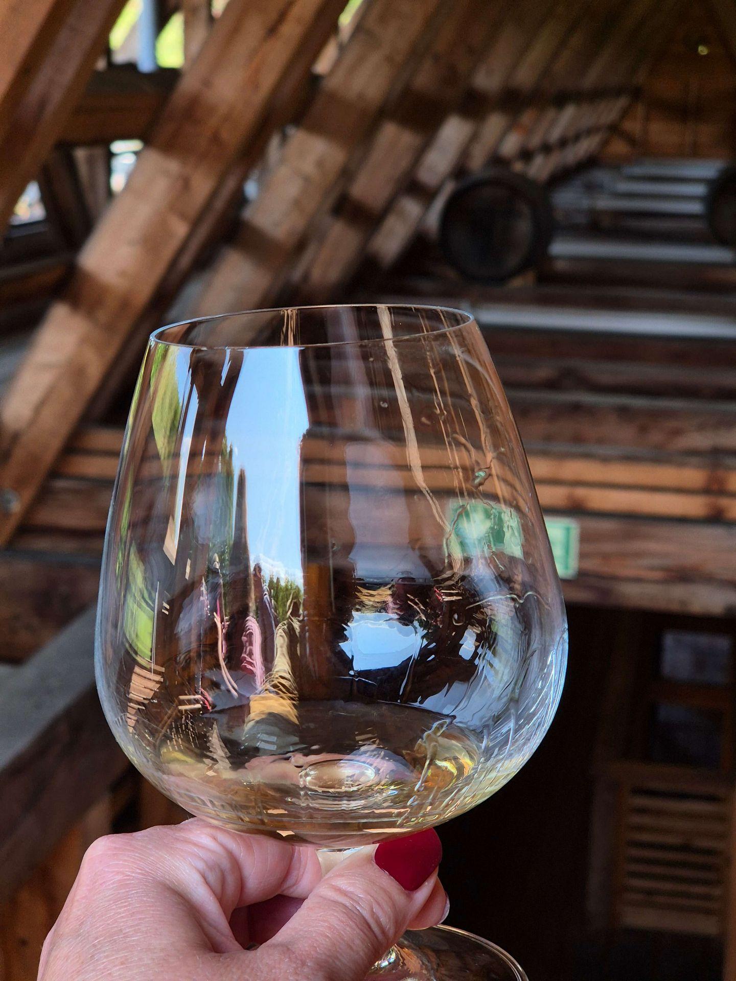 Hand hält ein bauchiges Whiskyglas mit einer kleinen Whiskyprobe vor der hölzernen Dachkonstruktion des Gradierwerks Bad Sassendorf.