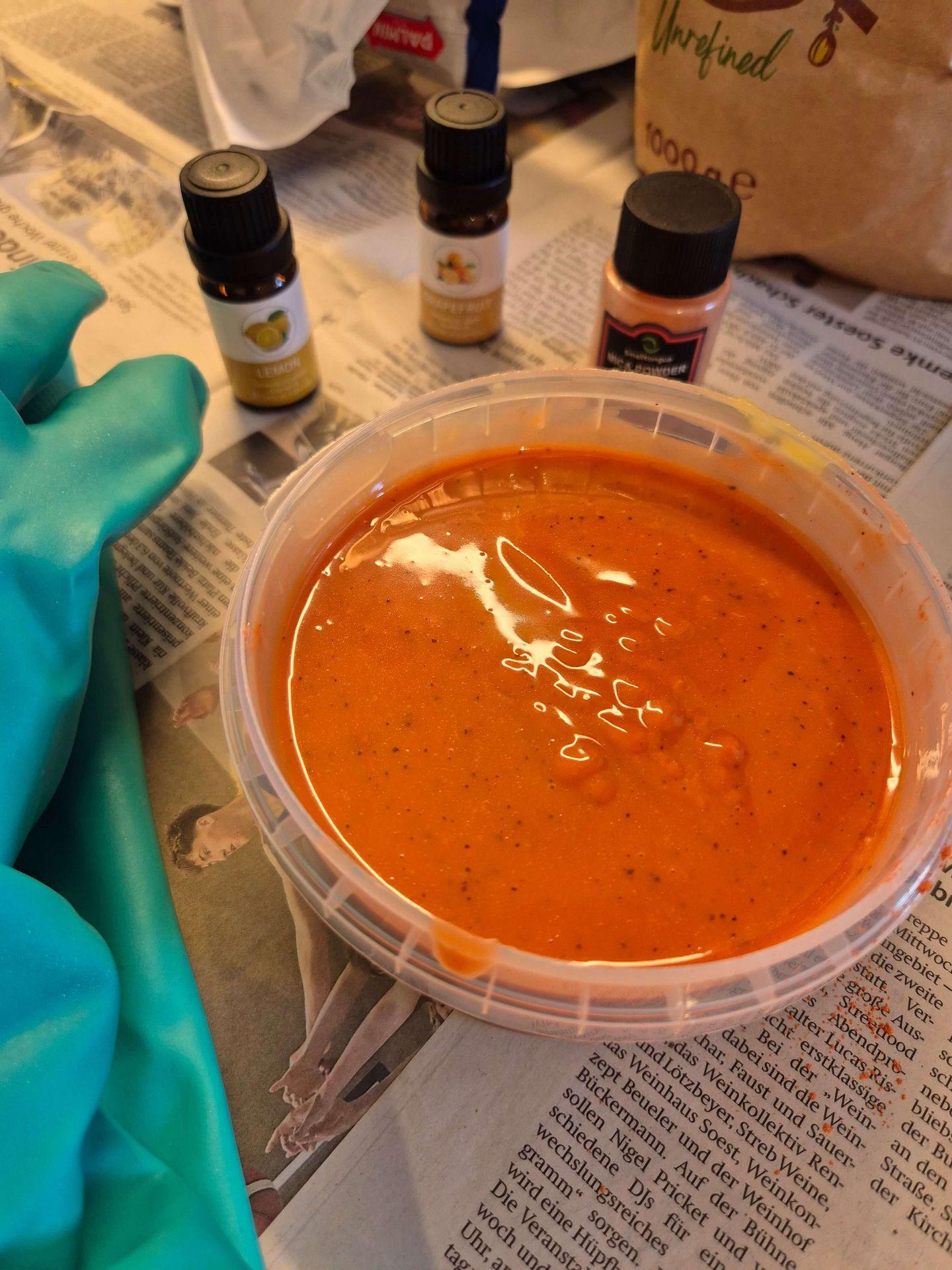 Orangefarbene Seifenmasse in einer Kunststoffschale mit Duftölen und Schutzhandschuhen beim Seifenworkshop in Bad Sassendorf.